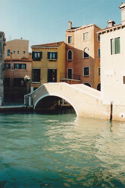 Stone bridge over a green canal between colorful houses in Venice