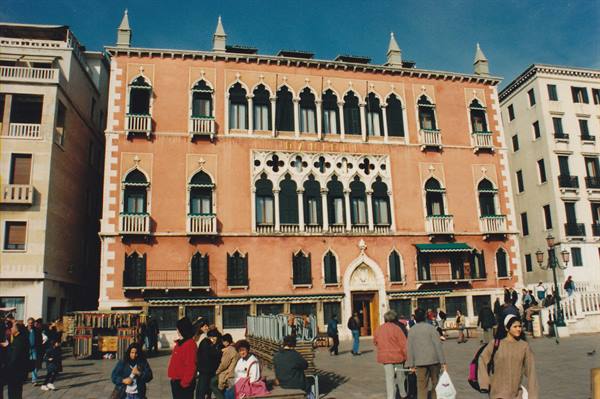 Tourists stroll past a salmon-pink Gothic facade in Venice