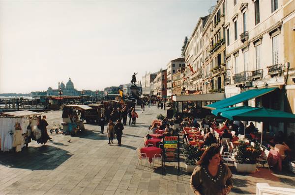 Riva degli Schiavoni in Venice: café with green umbrellas, strollers, Salute church beyond