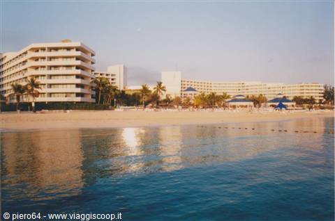 Beach with umbrellas in front of white hotels and palm trees, turquoise sea