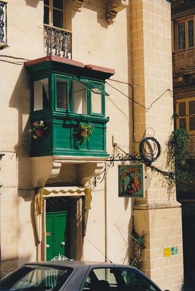 Traditional Maltese green wooden balcony on limestone facade, with pub sign