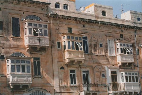 Traditional Maltese enclosed wooden balconies on sandstone facade, sunlight