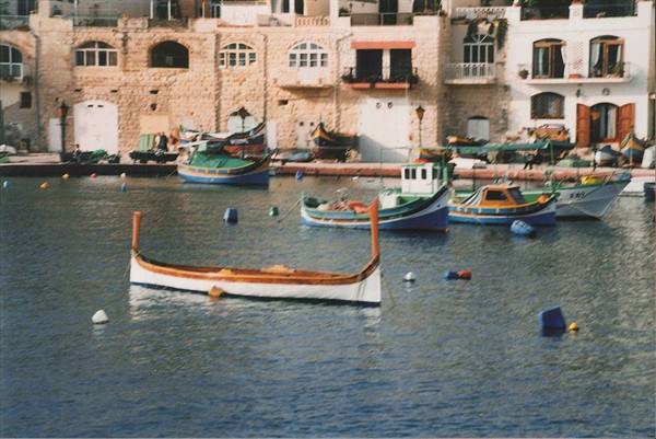 Colorful fishing boats moored by limestone houses at Spinola Bay