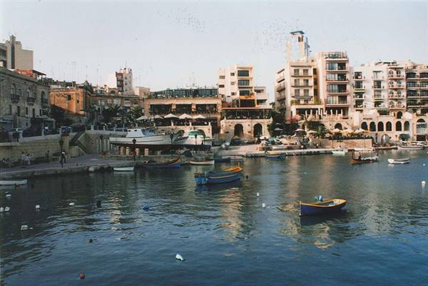 Colorful boats moored in Spinola Bay, buildings and restaurants along the waterfront