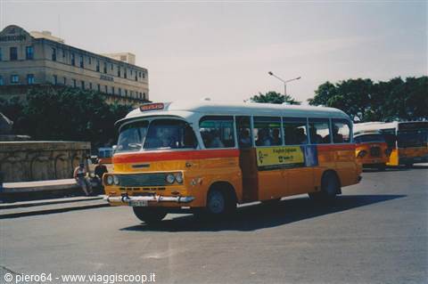 Yellow and white bus parked on a sunny square with buildings