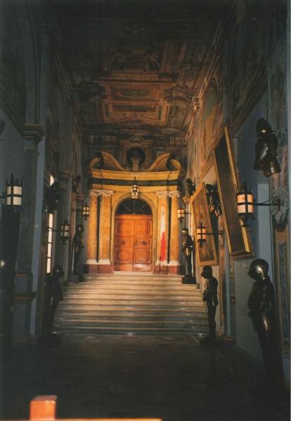 Marble staircase with gilded door, suits of armor and lit lanterns on walls