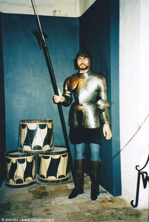 Medieval armor holding a halberd beside painted drums, blue walls