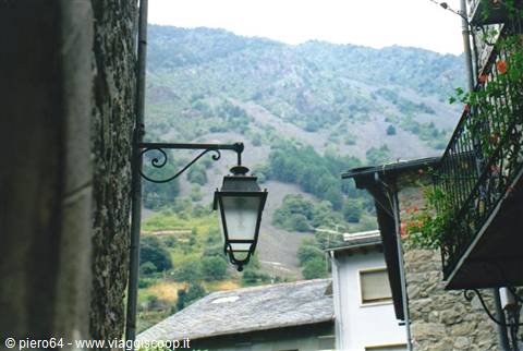 Black wrought-iron street lamp on stone wall, green mountains behind