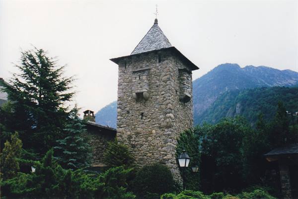 Stone tower with slate roof among conifers and mountains