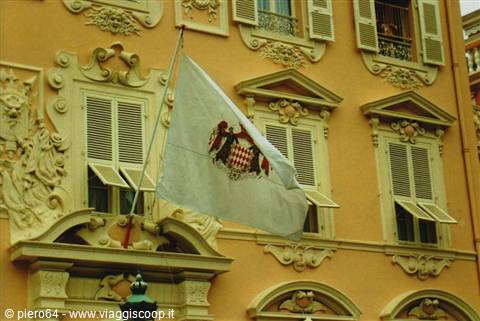 Monaco flag waving on ochre facade with stucco decorations and open shutters