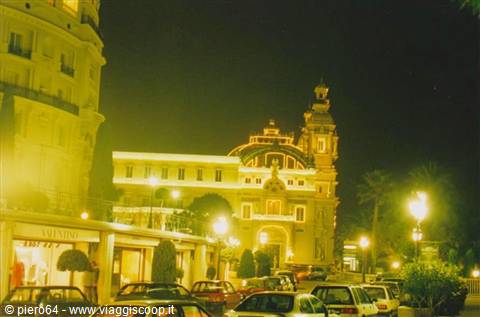 Monte Carlo Casino lit up at night, cars parked under street lamps