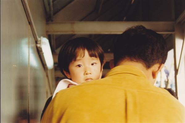 Child carried on a man's shoulders, man in yellow sweater under covered walkway