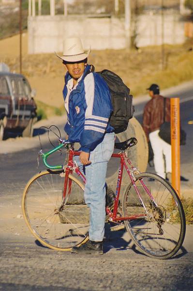Young man in straw hat with backpack standing beside a red bicycle