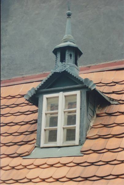 Wooden dormer window with metal spire over pink curved tiles