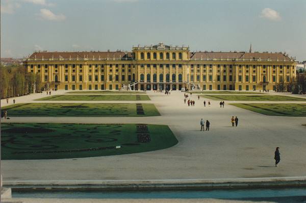 Yellow Schönbrunn palace with front gardens, visitors walk on gravel