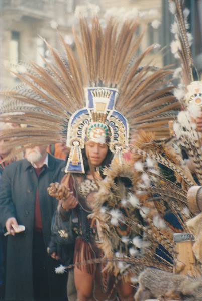 Aztec dancer wearing large brown feather headdress parading through the street