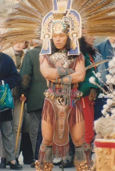 Aztec dancer wearing a large feathered headdress with crossed arms