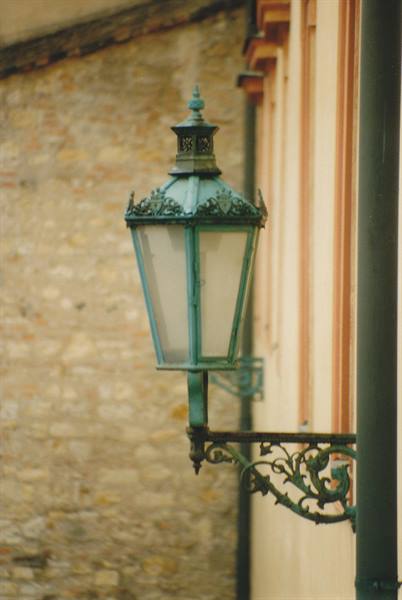 Oxidized green copper lantern on wrought iron bracket, stone wall in Prague