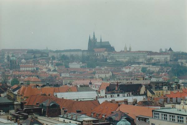 Prague Castle and St Vitus Cathedral rising above red rooftops in the haze
