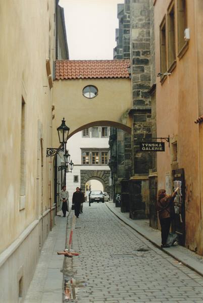 Cobbled alley with stone archway, Týnská Galerie sign, woman reading a board
