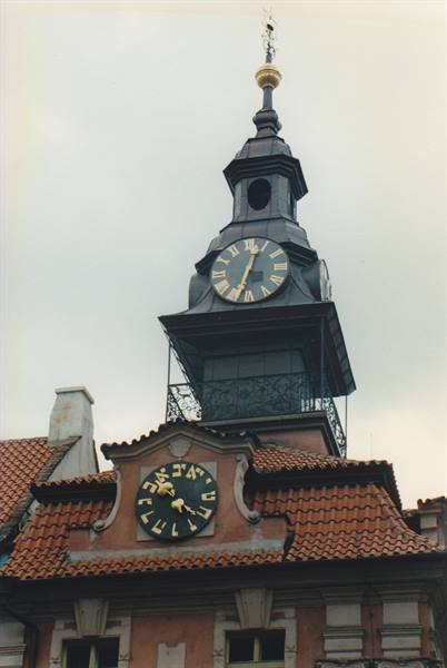 Clock tower with Hebrew dial above red tiled roofs in Prague
