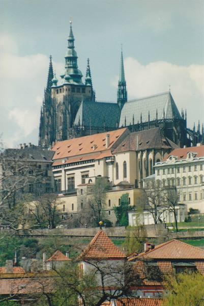 St. Vitus Cathedral rising above red rooftops and trees in Prague