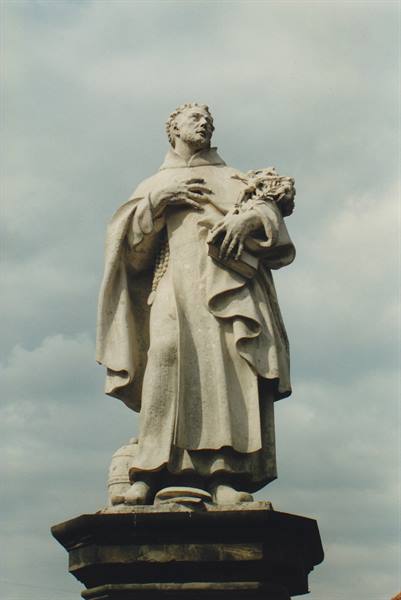Baroque stone statue of a saint holding a book, on pedestal under cloudy sky