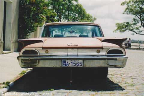 Old brown Ford Galaxie parked on cobblestones under midday sun