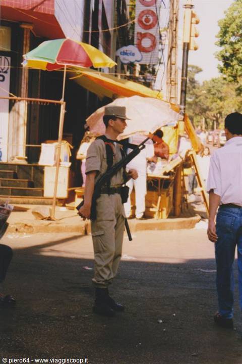 Soldier in uniform with rifle slung under colorful market umbrellas