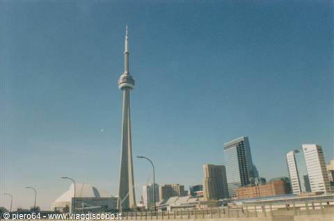 The CN Tower in Toronto rises above skyscrapers under a blue sky