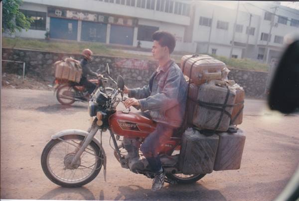 Man loading bundled bottles onto a red motorcycle on a Chinese town street