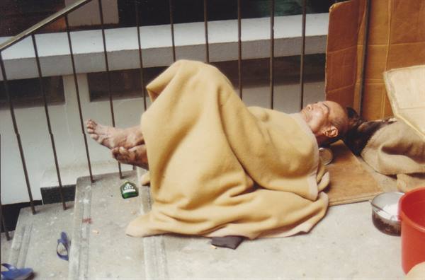 Elderly man sleeps wrapped in a yellow blanket on concrete steps by metal railings