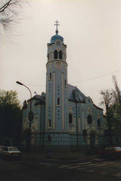 Blue church with pale blue bell tower and cross in Bratislava under grey sky