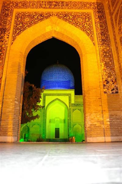 Ornate brick gateway frames an illuminated blue dome at night, Samarkand