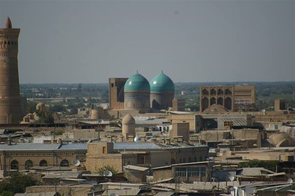 Bukhara: brick minaret and turquoise domes rising above old rooftops