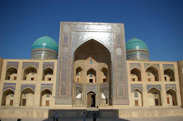 Madrasa with blue tiled portal and two turquoise domes, visitors walk in the square