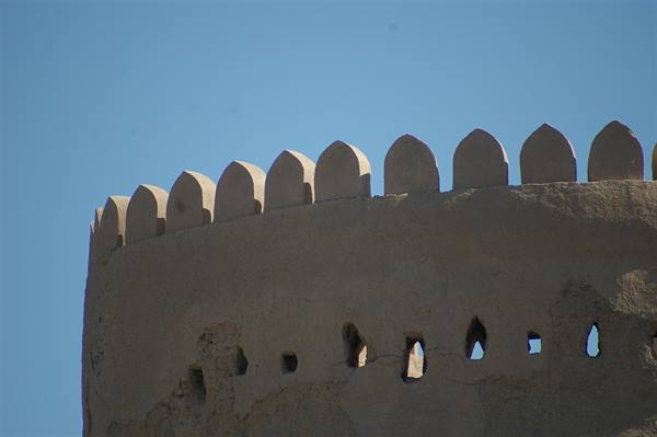 Mud-brick fortified tower, pointed crenellations and arrow slits against blue sky
