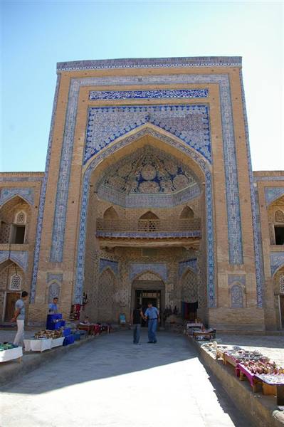Tourists before an ancient mausoleum decorated with blue tiles, bright sunlight