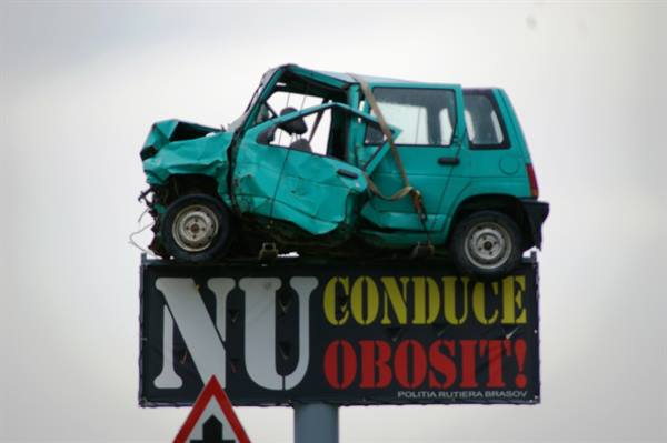 Crushed turquoise car mounted on a road safety billboard in Braşov