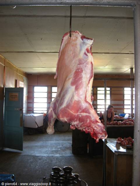 Hanging beef carcass in an indoor market hall, woman at the counters