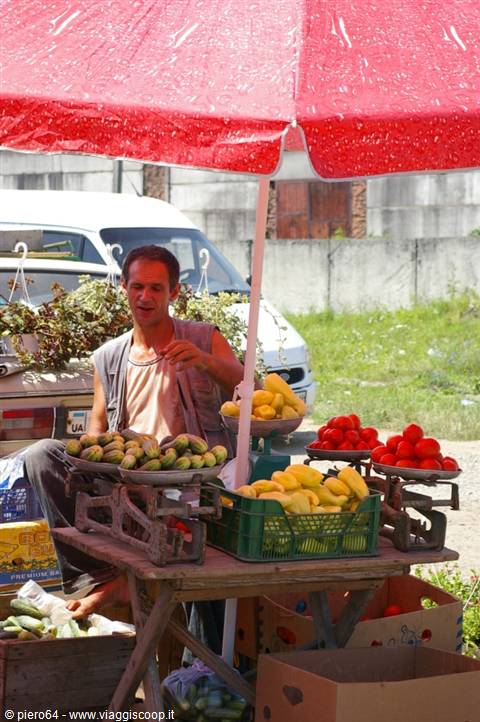 Vendor under red umbrella selling zucchinis, melons and tomatoes on scales