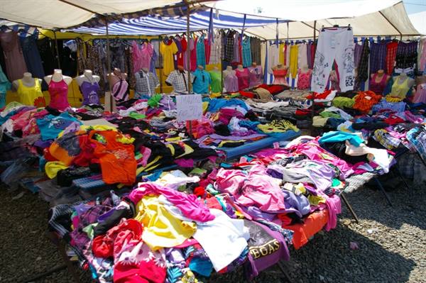 Colorful clothes piled on flea market stalls under white tents