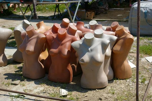Headless dressmaker mannequins clustered on dry grass at an outdoor flea market