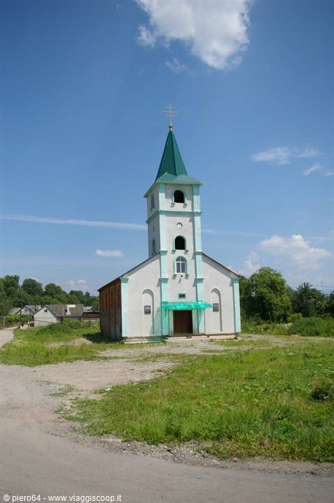 White church with green steeple and bell tower under blue cloudy sky