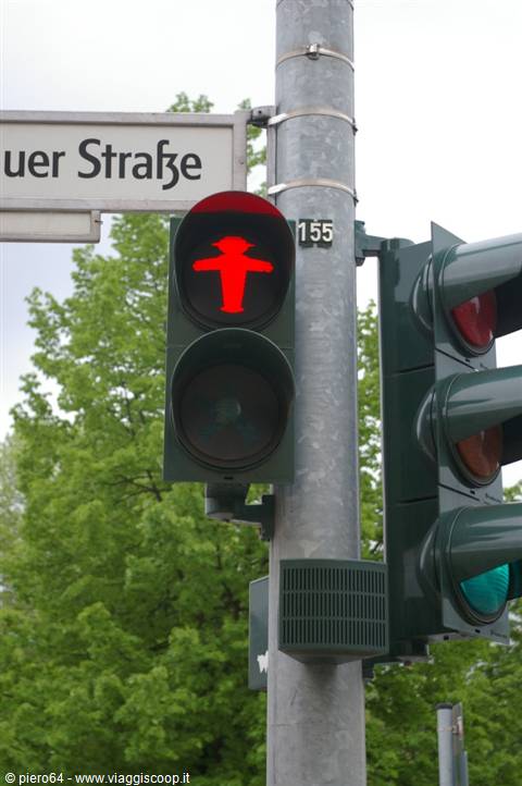 Pedestrian traffic light showing red figure, German street sign, green trees
