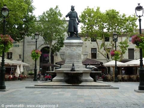 Bronze statue on stone fountain in Avignon square with cafés and lampposts
