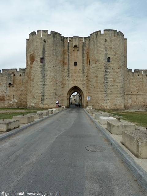 Stone fortified gate with round towers at Aigues-Mortes, person on the road