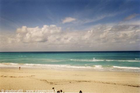 Pale sand beach, turquoise foamy sea, white clouds, few bathers