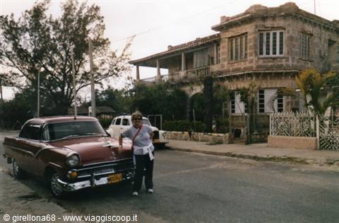 Woman beside a vintage car in front of a colonial villa, Havana