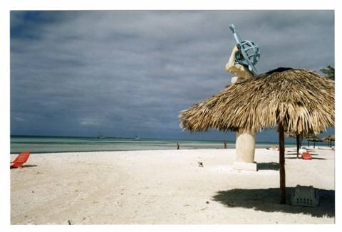 White sand beach with thatched umbrella and statue holding a ship's wheel